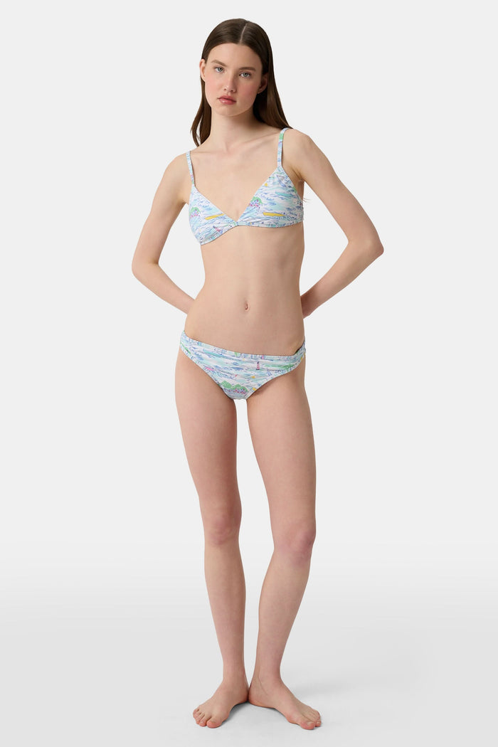 A person wears the Roller Rabbit Regatta Marais Bikini Bottom, featuring a colorful nautical print with boats and lighthouses. The UPF 50+ swimwear offers sun protection. Image is cropped from chest to upper thighs.