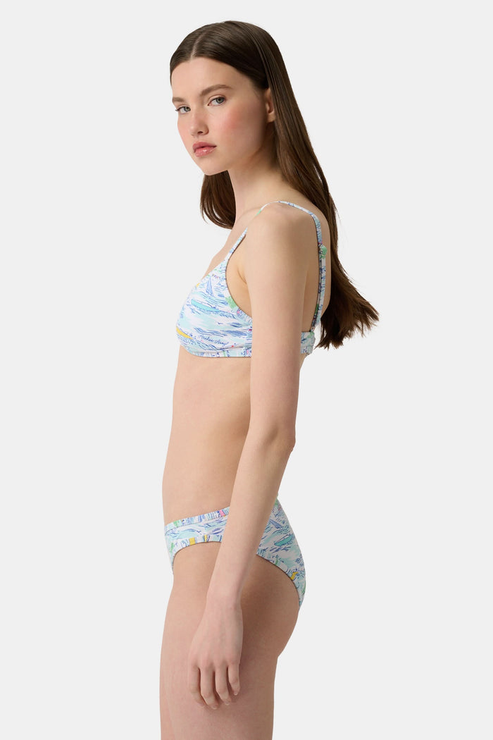 A person wears the Roller Rabbit Regatta Marais Bikini Bottom, featuring a colorful nautical print with boats and lighthouses. The UPF 50+ swimwear offers sun protection. Image is cropped from chest to upper thighs.