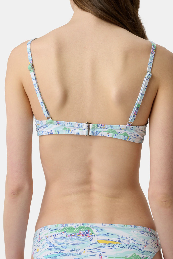 A woman with long brown hair smiles softly, wearing the Regatta Marais Bikini Top by Roller Rabbit in a nautical print, standing against a plain white background.