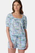 A woman wears the Roller Rabbit Regatta Preston Set, a cotton voile two-piece with a pastel coastal print, featuring a short-sleeve top with gathered neckline and matching shorts, standing against a plain white background.