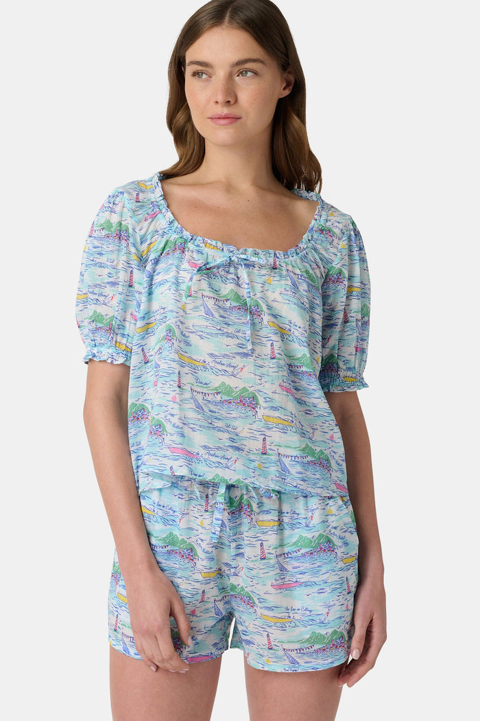 A woman wears the Roller Rabbit Regatta Preston Set, a cotton voile two-piece with a pastel coastal print, featuring a short-sleeve top with gathered neckline and matching shorts, standing against a plain white background.