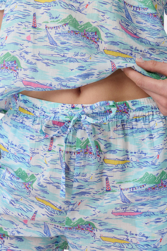 A woman wears the Roller Rabbit Regatta Preston Set, a cotton voile two-piece with a pastel coastal print, featuring a short-sleeve top with gathered neckline and matching shorts, standing against a plain white background.