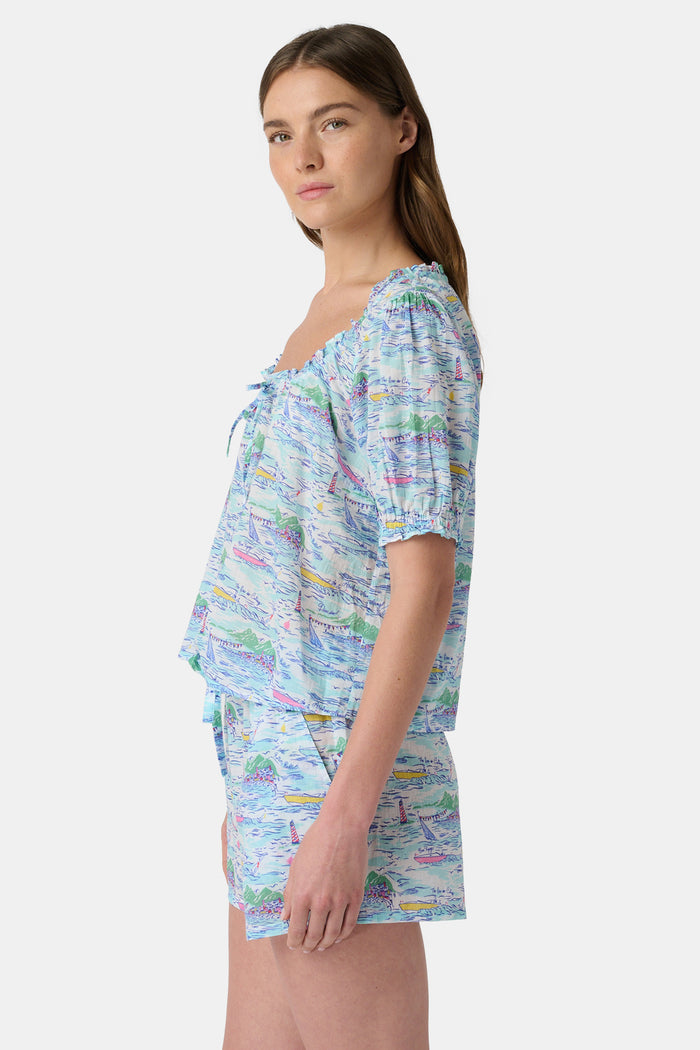 A woman wears the Roller Rabbit Regatta Preston Set, a cotton voile two-piece with a pastel coastal print, featuring a short-sleeve top with gathered neckline and matching shorts, standing against a plain white background.