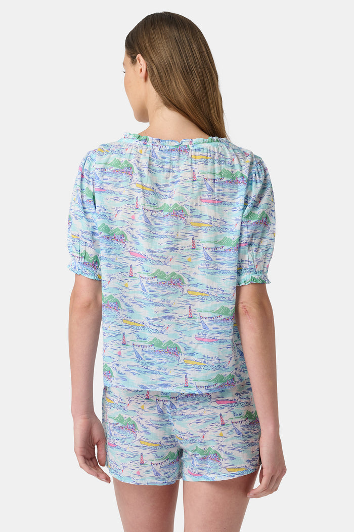 A woman wears the Roller Rabbit Regatta Preston Set, a cotton voile two-piece with a pastel coastal print, featuring a short-sleeve top with gathered neckline and matching shorts, standing against a plain white background.