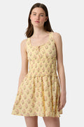 A young woman models the Roller Rabbit Rosa Ditsy Floral Penny Dress, a light yellow sundress with a floral pattern, gathered bodice, and gently flared skirt, set against a plain white background.