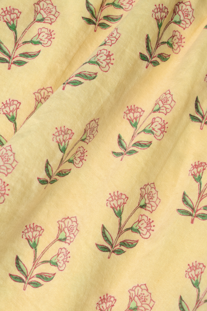 A young woman models the Roller Rabbit Rosa Ditsy Floral Penny Dress, a light yellow sundress with a floral pattern, gathered bodice, and gently flared skirt, set against a plain white background.
