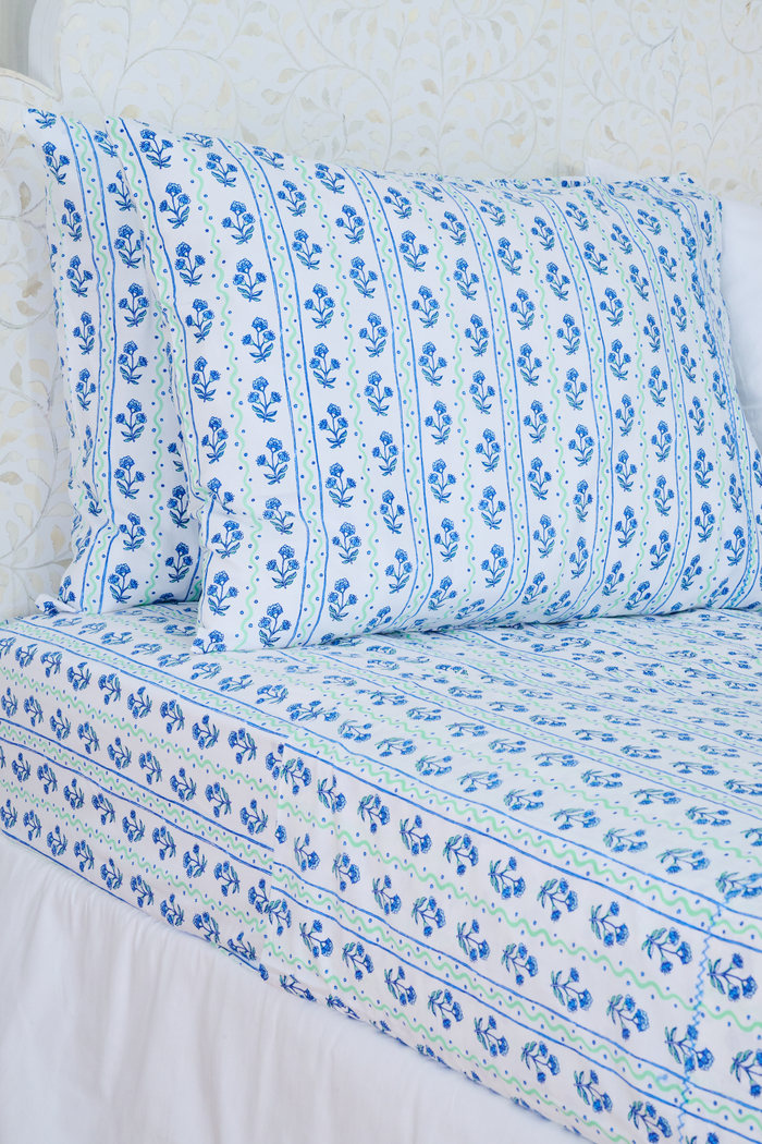 The Rosa Wavy Stripe Sheet Set by Roller Rabbit features a white sheet with blue floral print and green wavy stripes, ideal for twin XL beds or anyone seeking stylish cotton bedding.