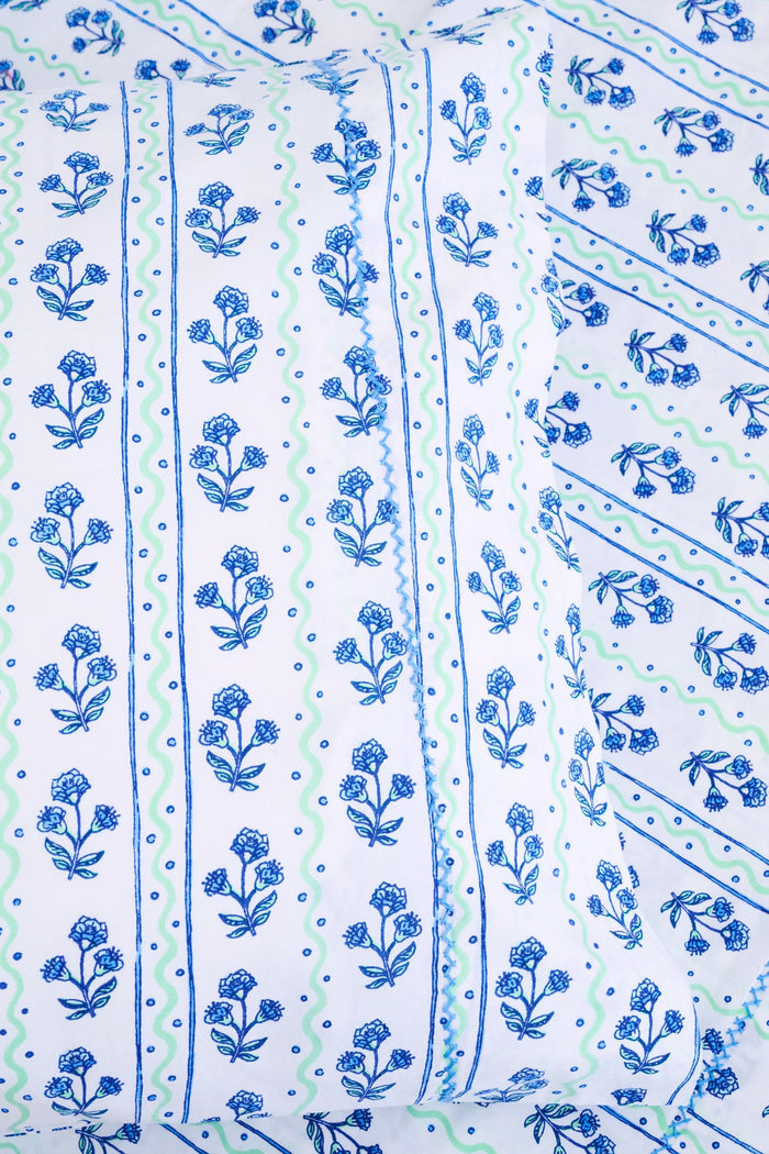 The Rosa Wavy Stripe Sheet Set by Roller Rabbit features a white sheet with blue floral print and green wavy stripes, ideal for twin XL beds or anyone seeking stylish cotton bedding.
