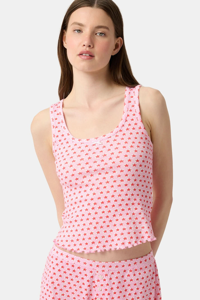 A young woman relaxes with a smile, lying on her back on a boat in the sun. She wears a bubblegum pink Starry Dot Astor Tank by Roller Rabbit and shorts, arms resting behind her head as the water glimmers nearby.
