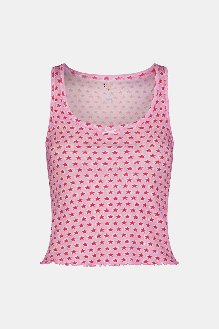 A young woman relaxes with a smile, lying on her back on a boat in the sun. She wears a bubblegum pink Starry Dot Astor Tank by Roller Rabbit and shorts, arms resting behind her head as the water glimmers nearby.