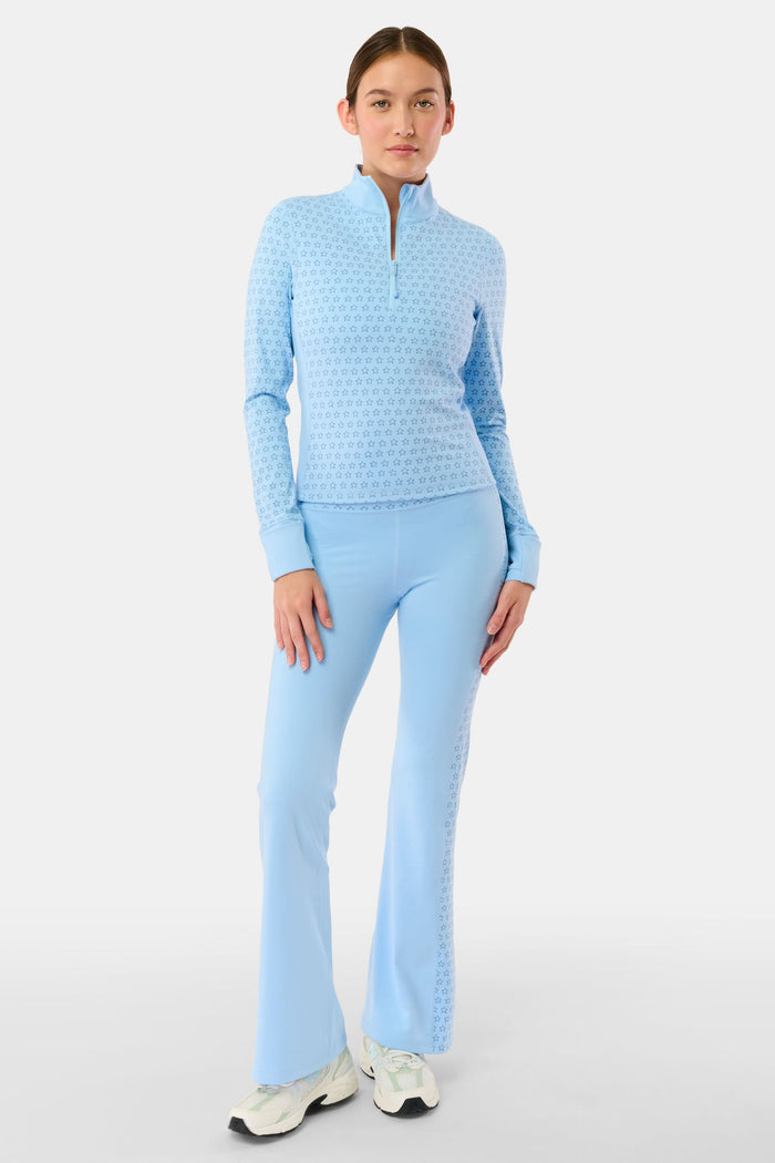 A person wearing Roller Rabbit's Stars Ally Flared Leggings in sky blue with a star print waistband, paired with a matching tied long-sleeve top and white sneakers. Only the lower body is visible.