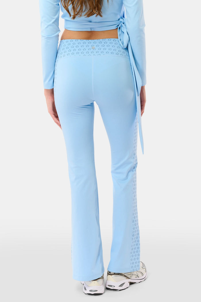 A person wearing Roller Rabbit's Stars Ally Flared Leggings in sky blue with a star print waistband, paired with a matching tied long-sleeve top and white sneakers. Only the lower body is visible.
