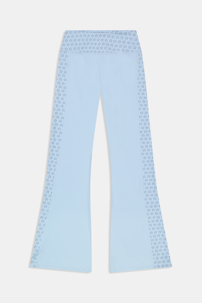 A person wearing Roller Rabbit's Stars Ally Flared Leggings in sky blue with a star print waistband, paired with a matching tied long-sleeve top and white sneakers. Only the lower body is visible.