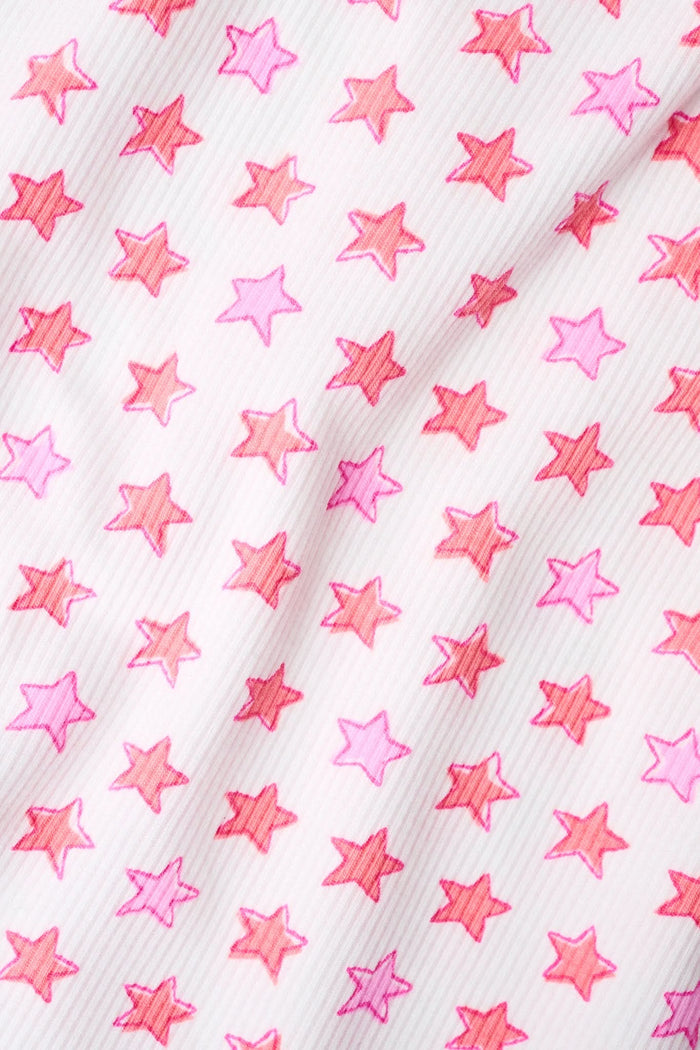 A person models the Roller Rabbit Stars Ann Rollover Shortie set—a matching ribbed tank top and cotton shorts with a coral star print, scalloped hem, and rollover waist—standing out against a plain, light background.