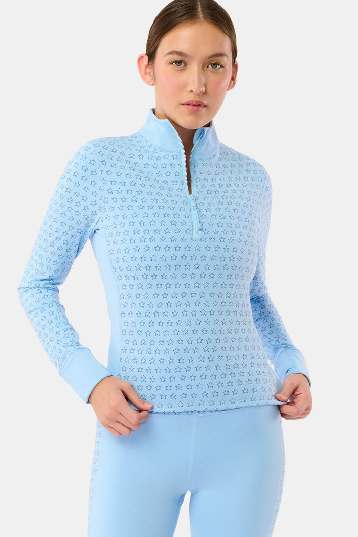 A woman wears the Roller Rabbit Stars Celia Quarter Zip in sky blue with a subtle star pattern and matching blue leggings, standing against a plain white background.