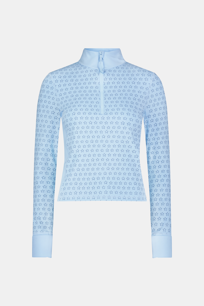 A woman wears the Roller Rabbit Stars Celia Quarter Zip in sky blue with a subtle star pattern and matching blue leggings, standing against a plain white background.