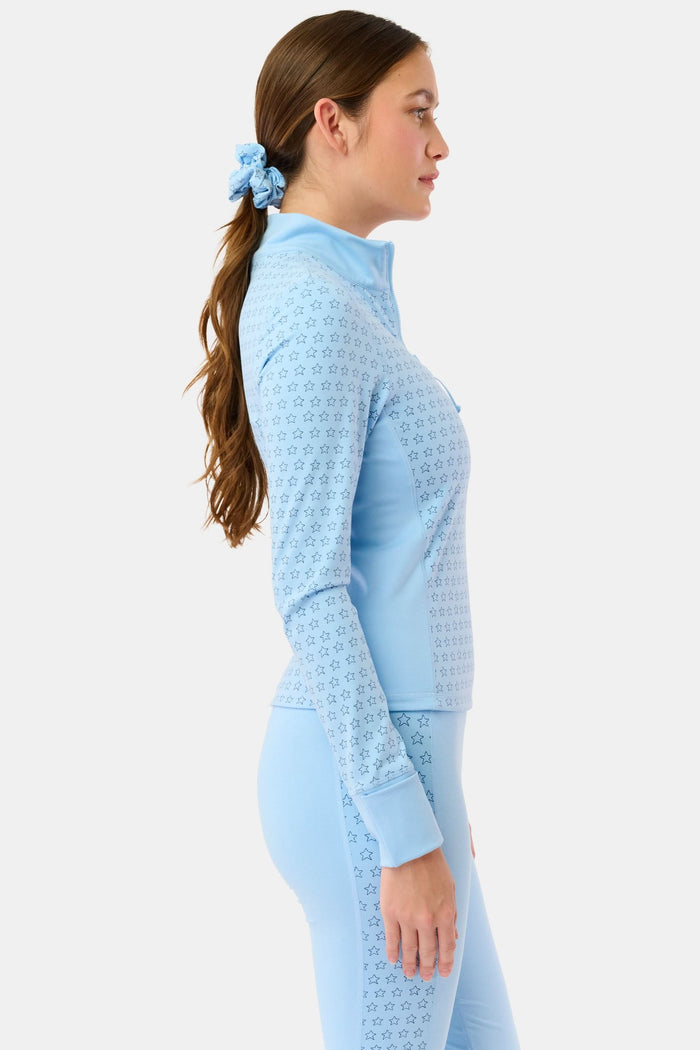 A woman wears the Roller Rabbit Stars Celia Quarter Zip in sky blue with a subtle star pattern and matching blue leggings, standing against a plain white background.