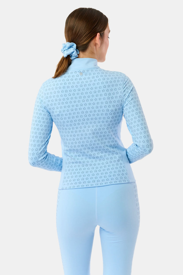 A woman wears the Roller Rabbit Stars Celia Quarter Zip in sky blue with a subtle star pattern and matching blue leggings, standing against a plain white background.