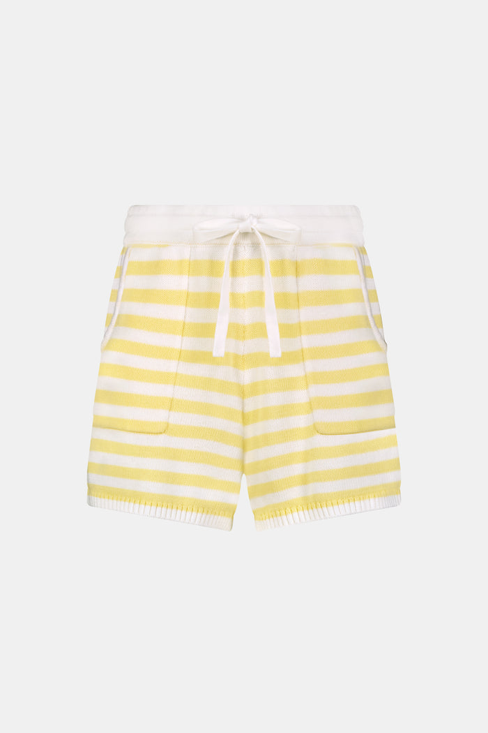 A person wears Roller Rabbit’s Striped Brie Short—a knit yellow and white horizontal striped short with a white drawstring at the elastic waistband and hands tucked in the front pockets.