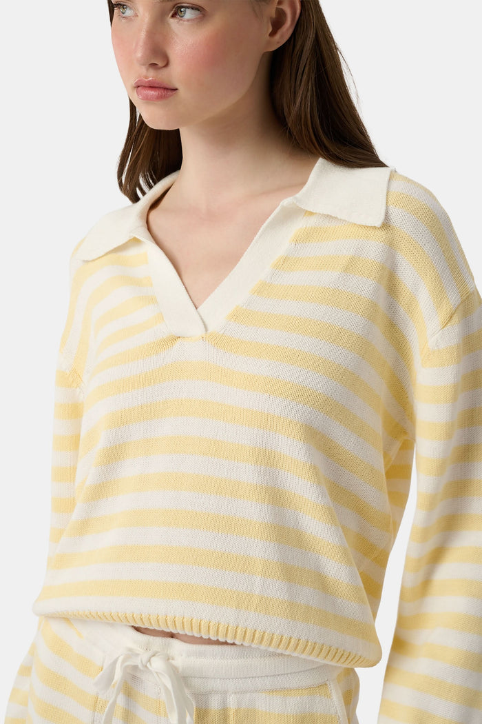 A young woman with light skin and long brown hair wears the Roller Rabbit Striped Rocio Sweater, a pastel yellow, lightweight cotton knit with a wide V-neck and collar. She pairs it with matching drawstring pants and gazes slightly to the side.