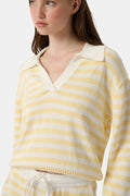 A young woman with light skin and long brown hair wears the Roller Rabbit Striped Rocio Sweater, a pastel yellow, lightweight cotton knit with a wide V-neck and collar. She pairs it with matching drawstring pants and gazes slightly to the side.