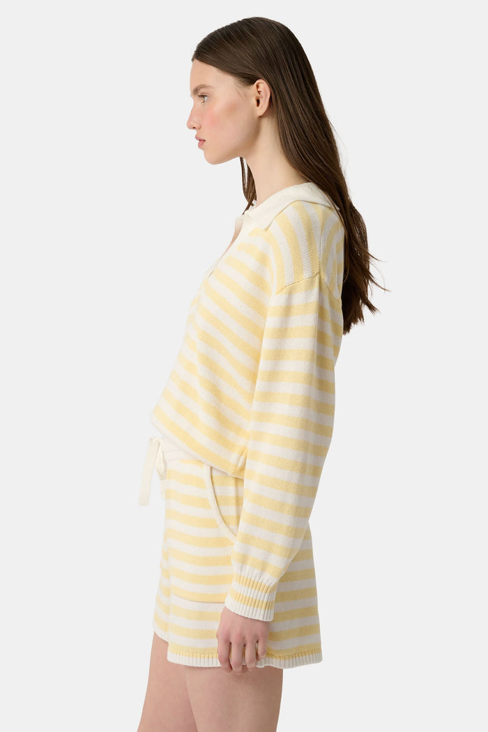 A young woman with light skin and long brown hair wears the Roller Rabbit Striped Rocio Sweater, a pastel yellow, lightweight cotton knit with a wide V-neck and collar. She pairs it with matching drawstring pants and gazes slightly to the side.