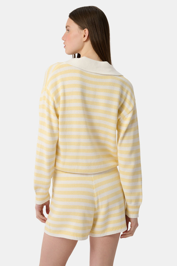 A young woman with light skin and long brown hair wears the Roller Rabbit Striped Rocio Sweater, a pastel yellow, lightweight cotton knit with a wide V-neck and collar. She pairs it with matching drawstring pants and gazes slightly to the side.