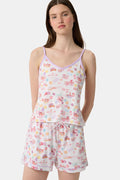 A woman wears the Roller Rabbit Summer Memories Mischa Set, a 100 Pima cotton cami tank and boxer set with a pastel travel icon print on white, standing against a light background.