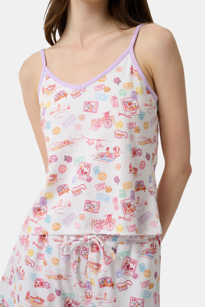 A woman wears the Roller Rabbit Summer Memories Mischa Set, a 100 Pima cotton cami tank and boxer set with a pastel travel icon print on white, standing against a light background.