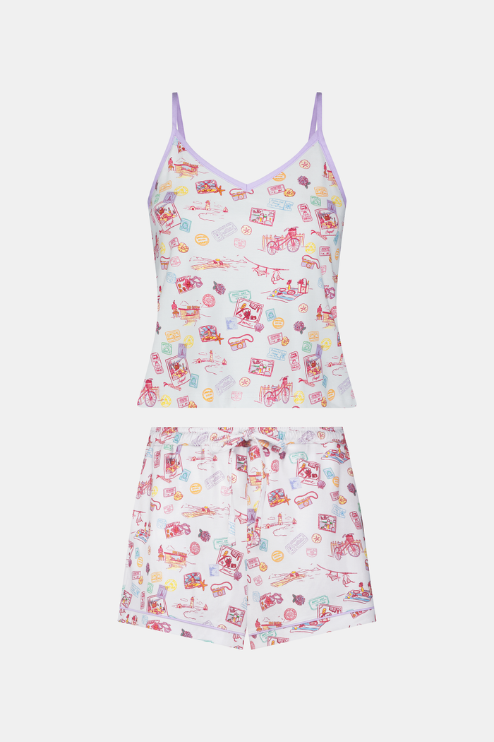 A woman wears the Roller Rabbit Summer Memories Mischa Set, a 100 Pima cotton cami tank and boxer set with a pastel travel icon print on white, standing against a light background.