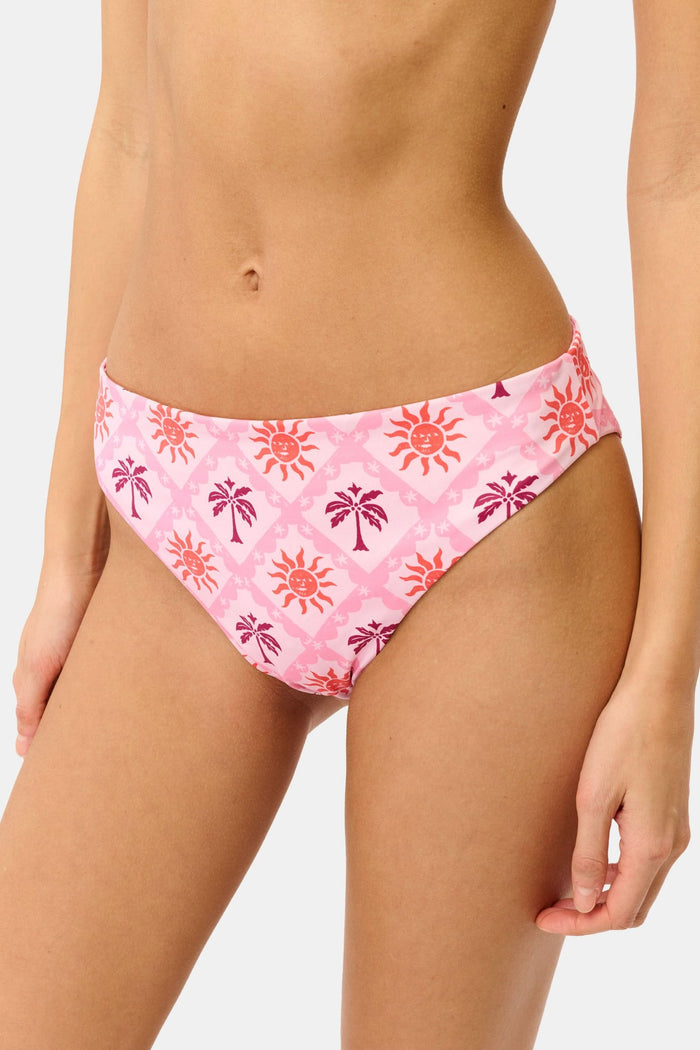 A model wears the Roller Rabbit Sunny Days Shelly Bikini Bottom, featuring orange and purple sun and palm tree patterns, shown from mid-torso to upper thigh against a plain background.