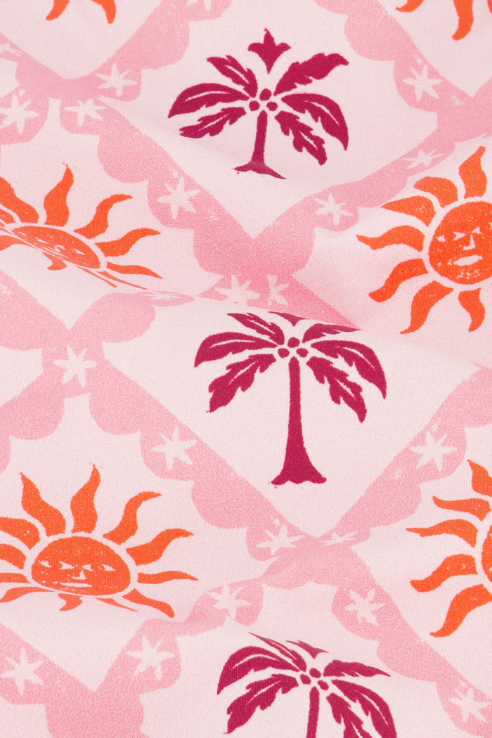 A model wears the Roller Rabbit Sunny Days Shelly Bikini Bottom, featuring orange and purple sun and palm tree patterns, shown from mid-torso to upper thigh against a plain background.
