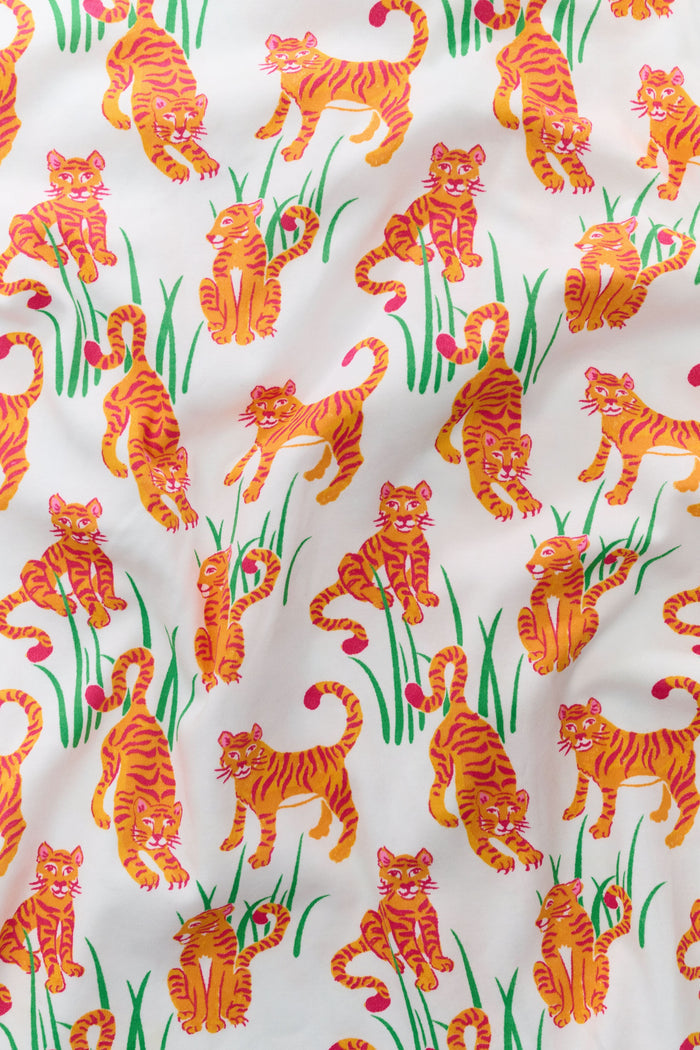 A person wears Roller Rabbit's Teddy Tiger Polo Pajamas, a matching short-sleeve set in 100 Pima Cotton, featuring a green plant and tiger print on white. They stand and smile slightly.