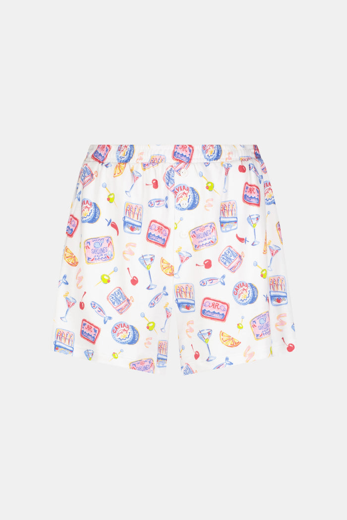 A person stands barefoot in the Roller Rabbit Tinned or Twist Brooklyn Boxer, a white pajama bottom with playful food and drink prints and a comfy elastic waistband. Only the lower half of the body is shown against a plain background.