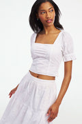 A woman wearing the Roller Rabbit Vanna Embroidery Kayla Top, a white blouse with short sleeves and a square neckline, paired with a matching high-waisted skirt, stands against a plain white background.
