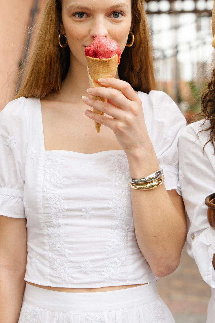 A woman wearing the Roller Rabbit Vanna Embroidery Kayla Top, a white blouse with short sleeves and a square neckline, paired with a matching high-waisted skirt, stands against a plain white background.