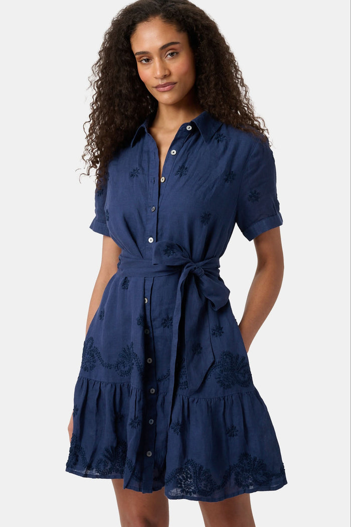 A woman models the Roller Rabbit Vanna Embroidery Margaret Dress—a short-sleeve navy linen shirtdress with a belted waist—standing against a plain light background.