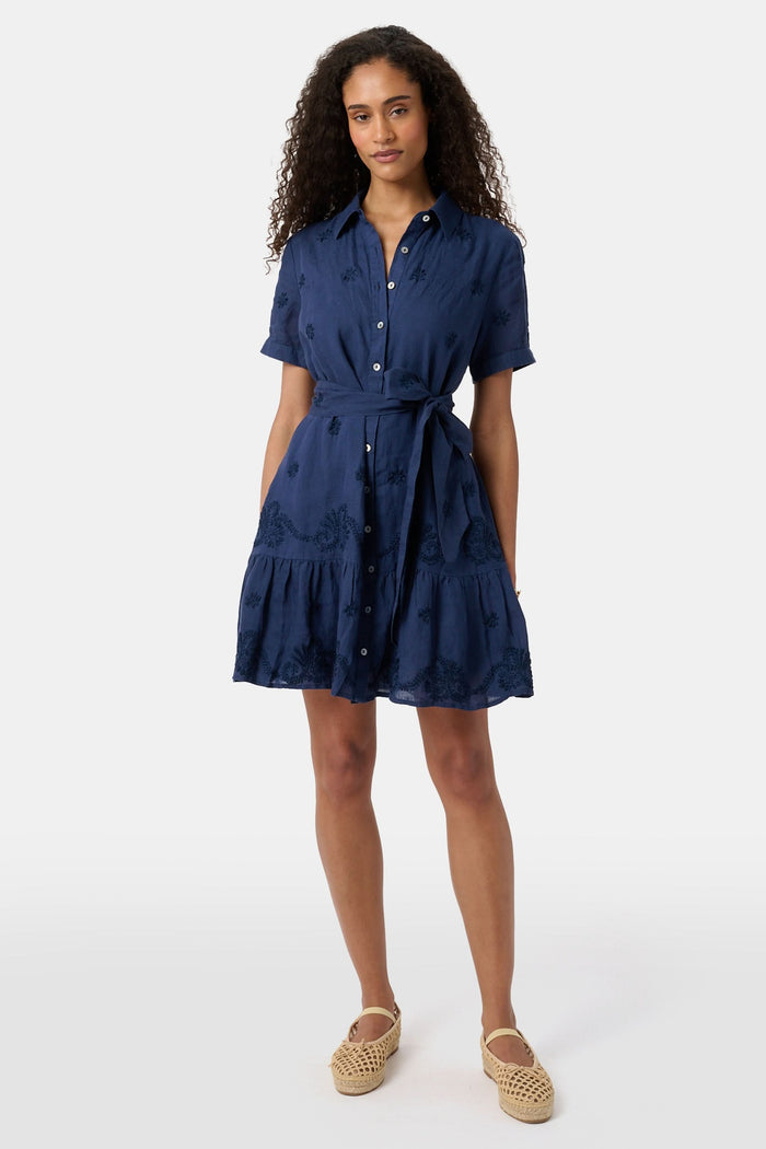 A woman models the Roller Rabbit Vanna Embroidery Margaret Dress—a short-sleeve navy linen shirtdress with a belted waist—standing against a plain light background.