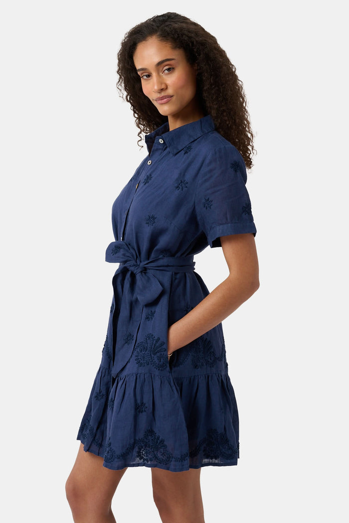 A woman models the Roller Rabbit Vanna Embroidery Margaret Dress—a short-sleeve navy linen shirtdress with a belted waist—standing against a plain light background.