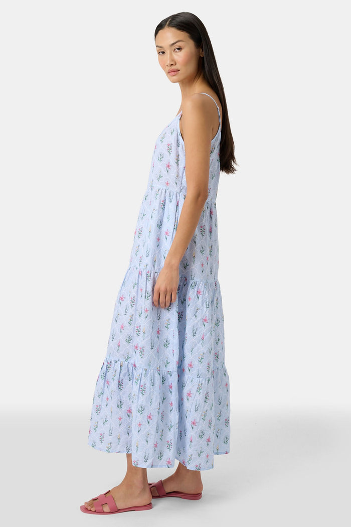 A woman with long hair stands facing forward, wearing the Roller Rabbit Wildflower Jemina Dakota Dress in sky blue and pink sandals.
