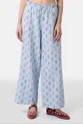 A person wears the Roller Rabbit Wildflower Jemina Lynette Pant—wide-leg, light blue summer pants with a Wildflower Trellis print and drawstring waist—paired with maroon flats featuring white floral designs.
