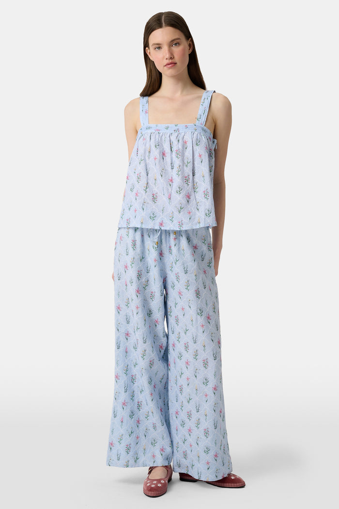 A person wears the Roller Rabbit Wildflower Jemina Lynette Pant—wide-leg, light blue summer pants with a Wildflower Trellis print and drawstring waist—paired with maroon flats featuring white floral designs.