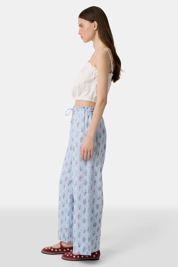 A person wears the Roller Rabbit Wildflower Jemina Lynette Pant—wide-leg, light blue summer pants with a Wildflower Trellis print and drawstring waist—paired with maroon flats featuring white floral designs.