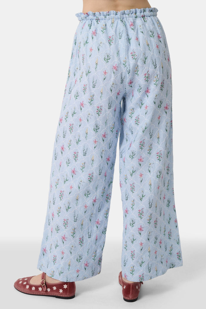 A person wears the Roller Rabbit Wildflower Jemina Lynette Pant—wide-leg, light blue summer pants with a Wildflower Trellis print and drawstring waist—paired with maroon flats featuring white floral designs.