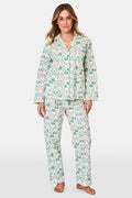 A woman stands barefoot in Roller Rabbit's Woodland Toile Loungewear, a cotton pajama set with a matching long-sleeve button-up top and pants in a green toile print. She faces forward, smiling slightly.