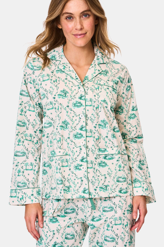 A woman stands barefoot in Roller Rabbit's Woodland Toile Loungewear, a cotton pajama set with a matching long-sleeve button-up top and pants in a green toile print. She faces forward, smiling slightly.